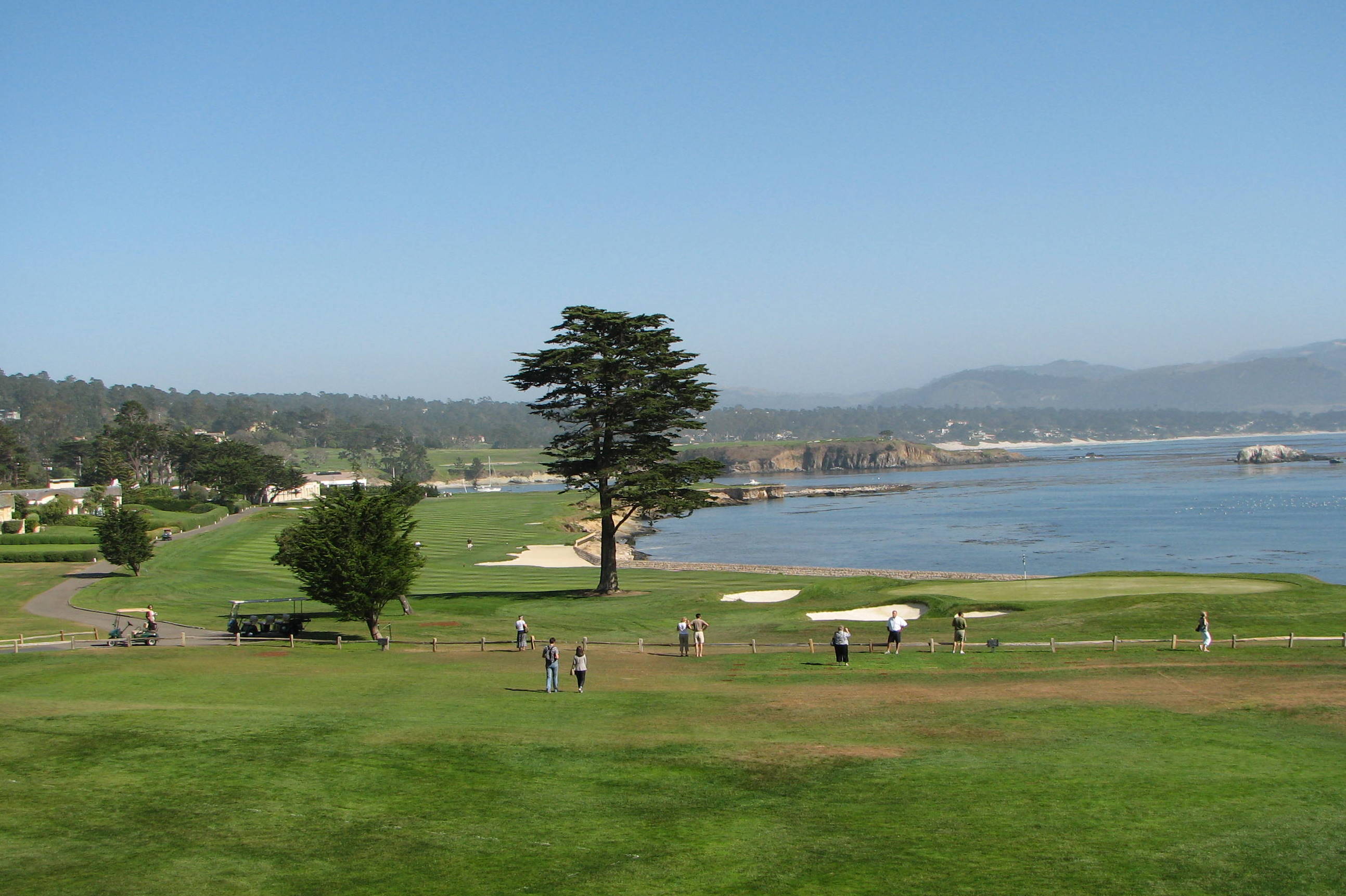 Fairway, green, bunkers, and Monterey Cypress at the 18th hole of Pebble Beach Golf Links beside Stillwater Cove